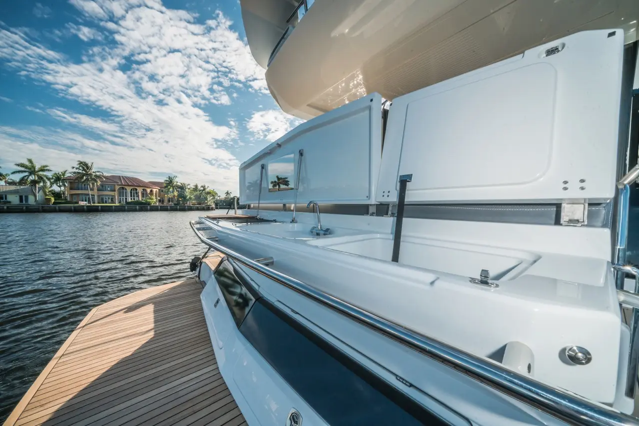 Luxury yacht terrace with a white sink area, wooden deck, and scenic waterfront view of palm trees and upscale homes.