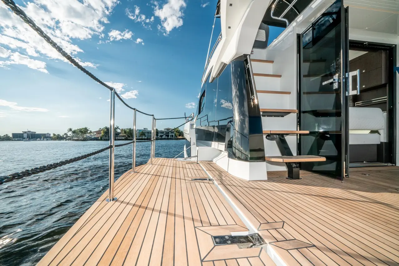 A luxury yacht's deck showcasing polished wood, a staircase, and expansive views of the water and distant homes under a blue sky.