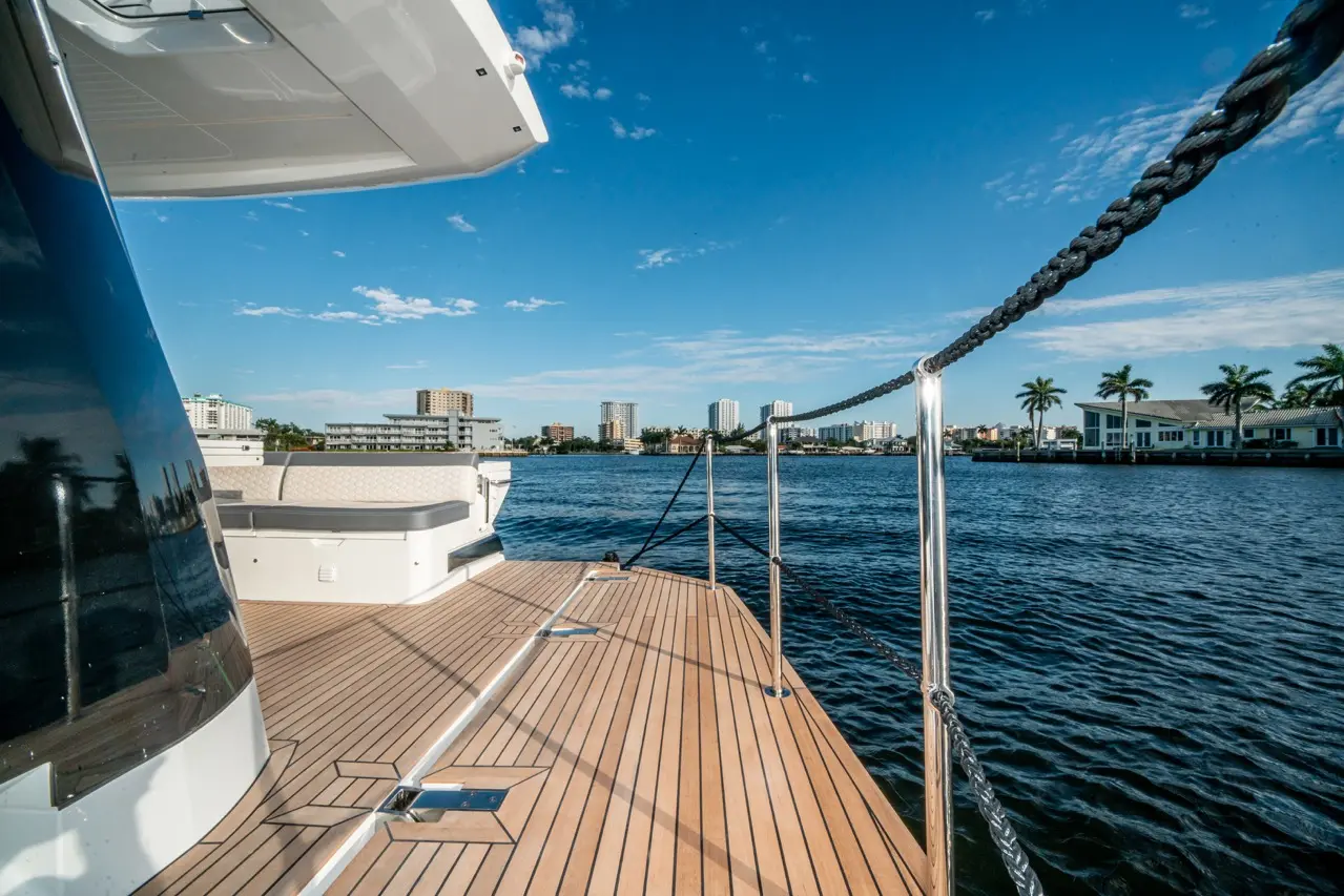 View from a yacht deck featuring a wooden surface, water, and buildings under a clear blue sky with scattered clouds.