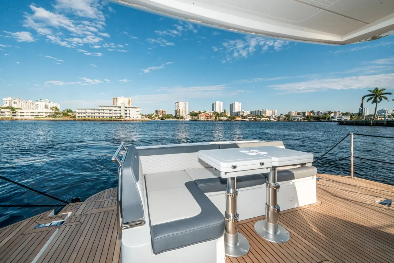 View from a luxury yacht showing seating area and table, with a waterfront city skyline under a blue sky and clouds.