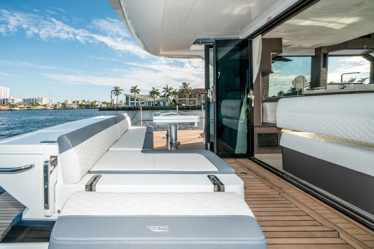 Luxury yacht deck with cushioned seating, a stainless steel table, and waterfront views featuring palm trees and modern homes.
