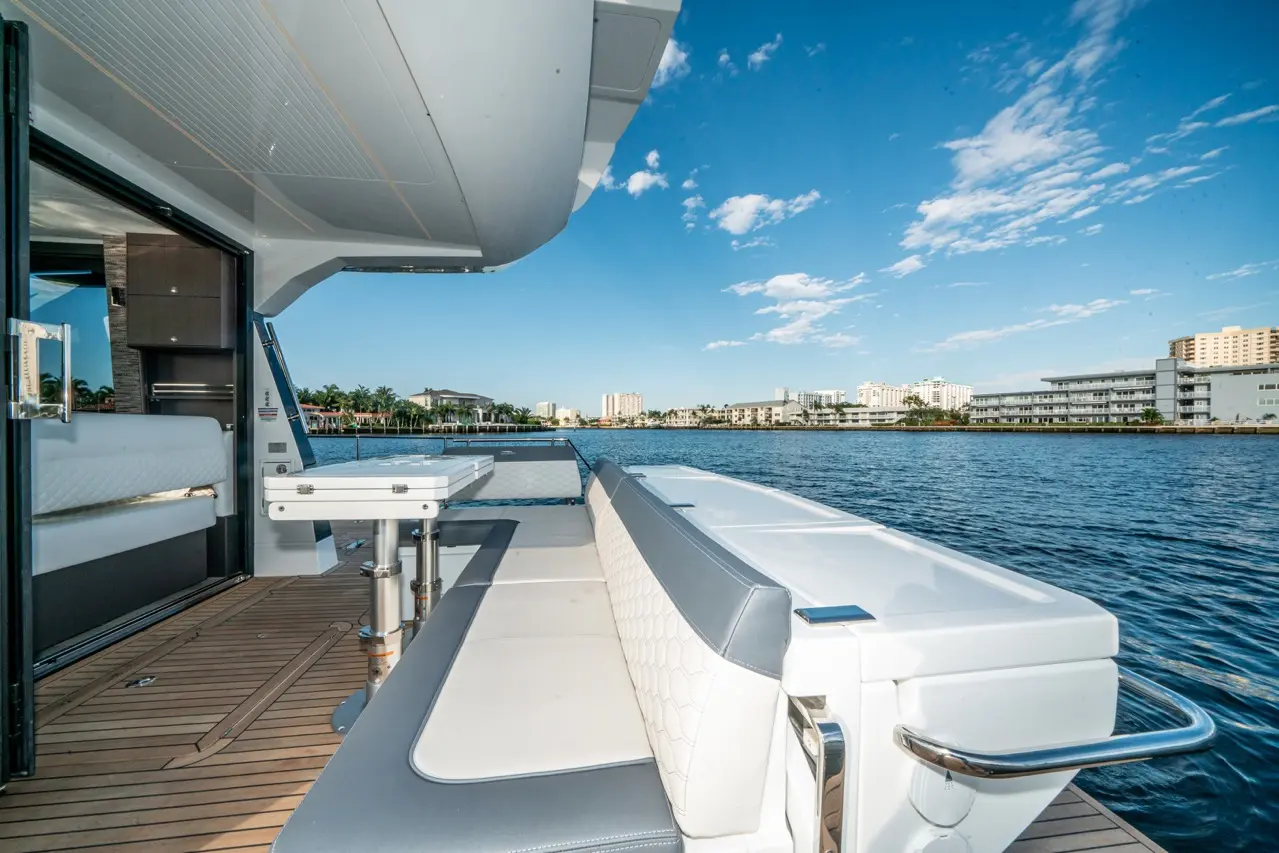 View from a luxury yacht's deck, featuring seating area and table, overlooking the water and waterfront buildings under blue sky.