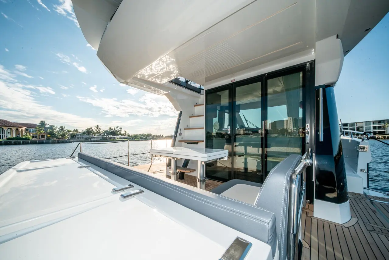 Luxury yacht deck with a dining table, modern seating, and glass doors overlooking a scenic waterfront view.