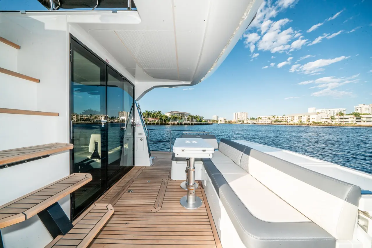 Luxurious boat deck overlooking water, featuring wooden steps, a seating area, and a portable table under a clear blue sky.