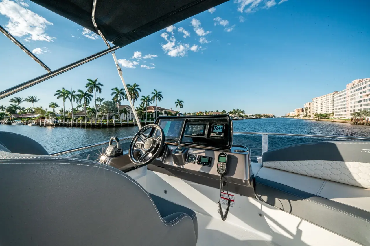 Boat cockpit view overlooking a canal lined with palm trees and waterfront homes, featuring navigation screens and a steering wheel.