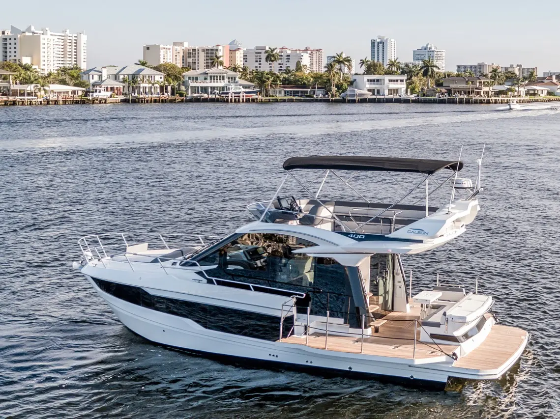 Luxury Galeon 400 yacht cruising on a waterway, modern buildings and palm trees in the background, showcasing boating lifestyle.