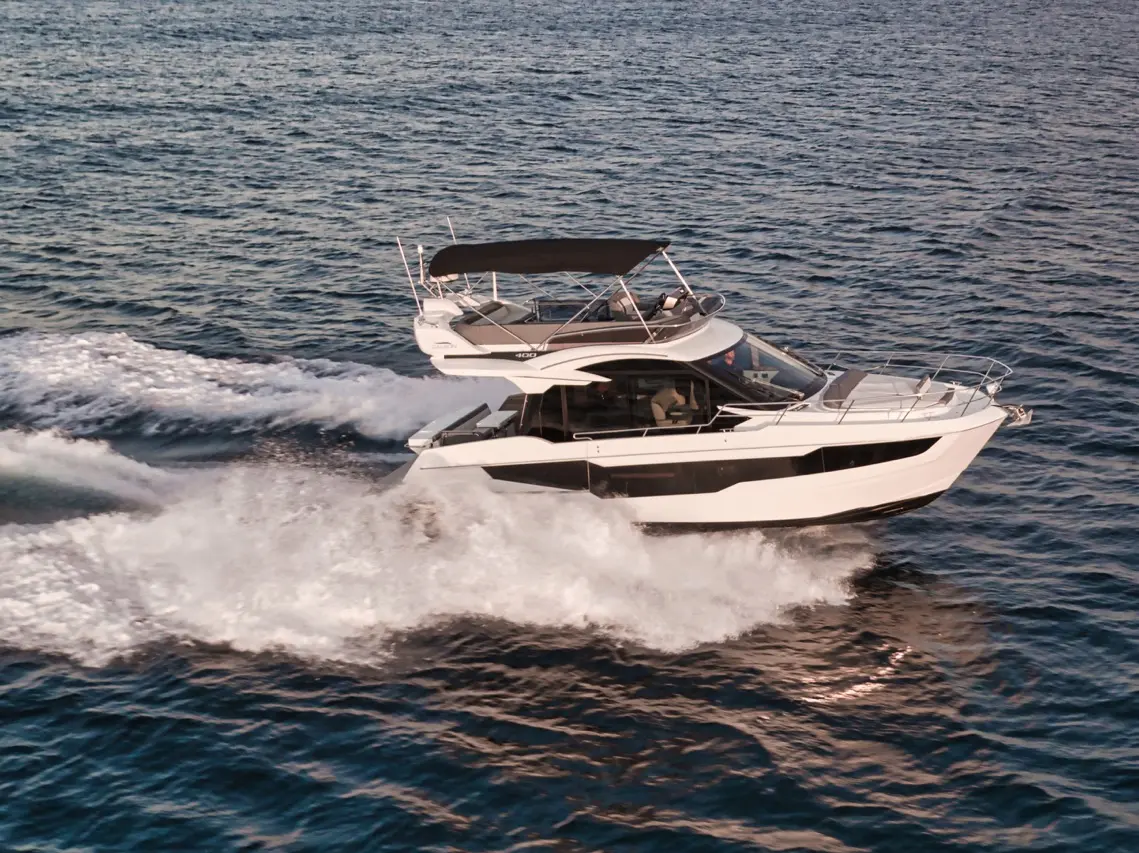 A sleek white motor yacht cruising through blue waters, creating waves and spray under a clear sky.