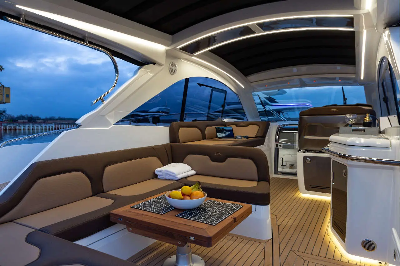 Luxury yacht interior with seating, fruit bowl, and ambient lighting, showcasing a modern design against a twilight sky.
