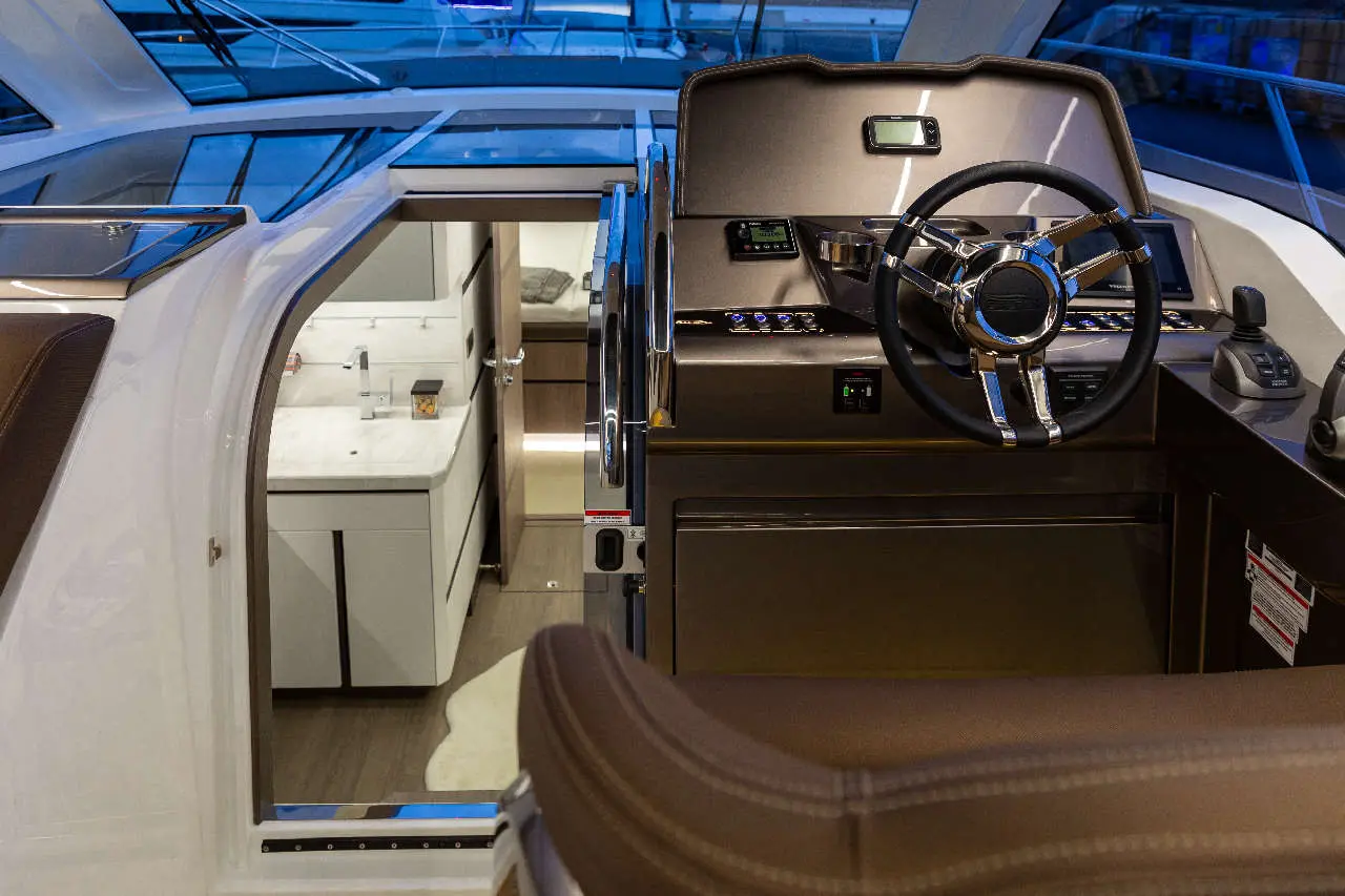 Luxury yacht interior showing a sleek steering wheel, console controls, and an adjacent cabin with modern amenities.