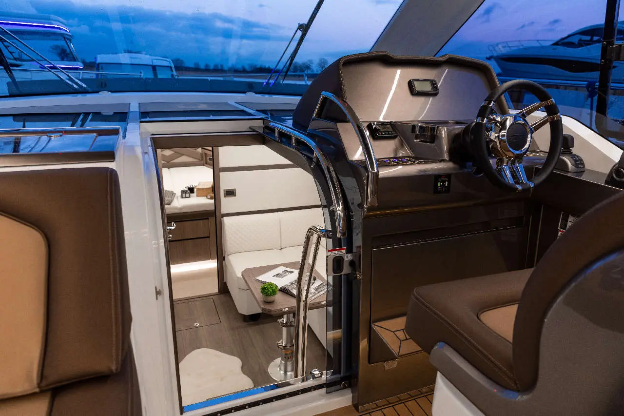 Interior of a luxury boat featuring a modern helm, seating area, and doorway to the living space, set in evening light.