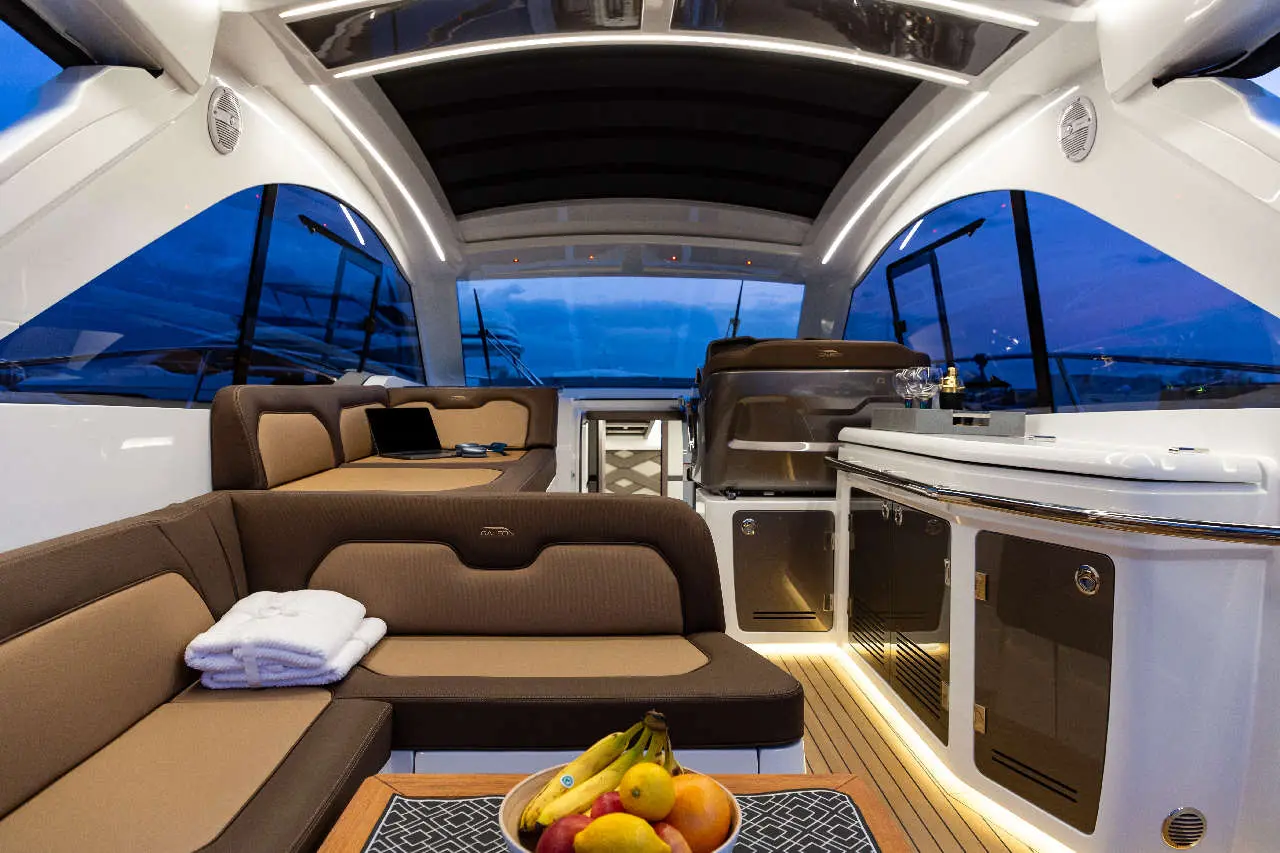 Luxury yacht interior featuring cozy seating, a fruit bowl on a table, and large windows showcasing a twilight view.