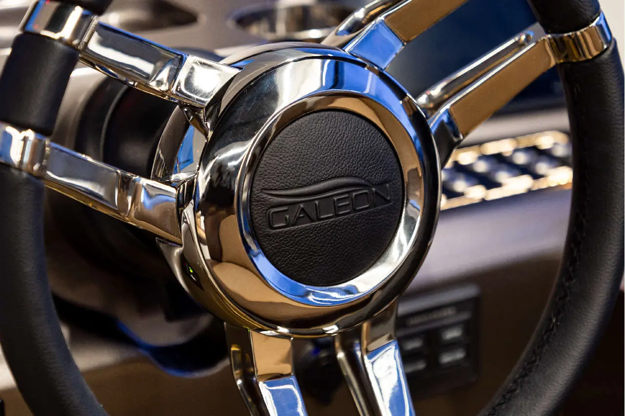 Close-up of a chrome steering wheel with a textured black center featuring the logo 