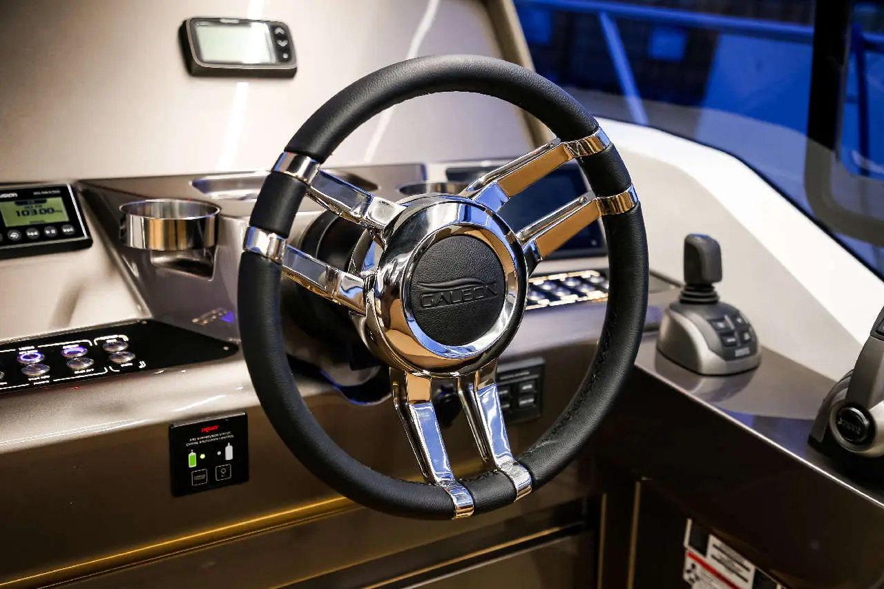 A close-up of a sleek boat steering wheel, featuring chrome detailing and control panel with gauges and buttons.
