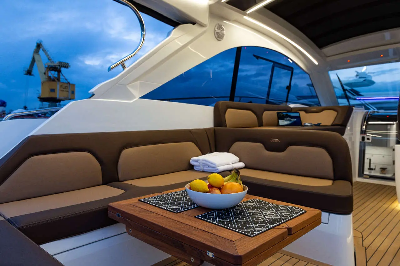 Luxurious yacht interior showing a cozy seating area with a bowl of fruit on a table, towels, and a view of the harbor.