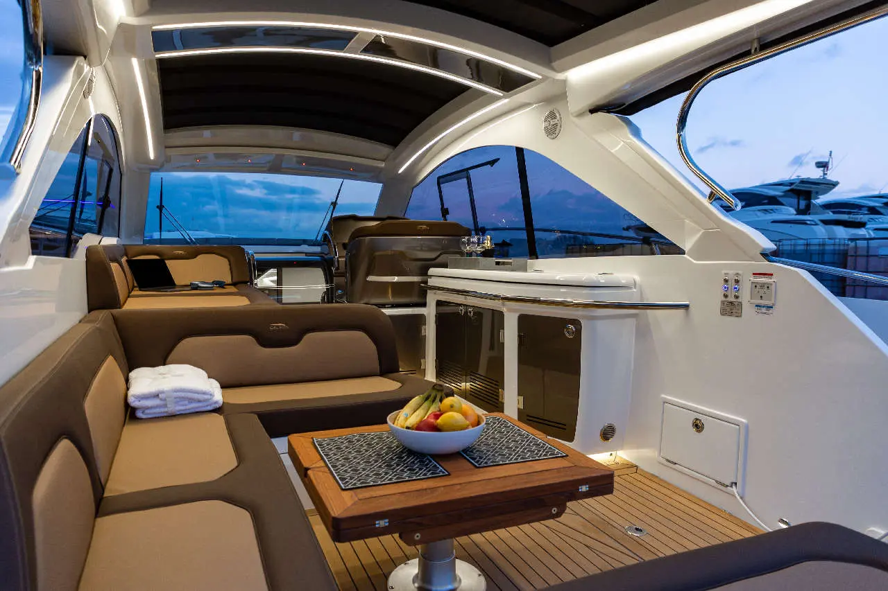 Luxurious yacht interior featuring cozy seating, a fruit bowl on a wooden table, and large windows showcasing the ocean view.