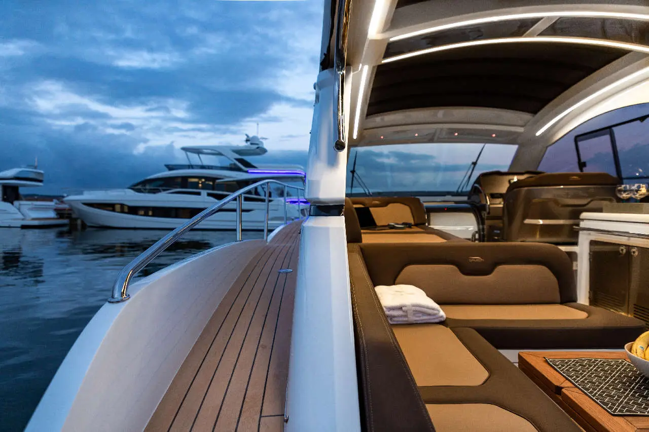 Modern yacht interior at dusk, featuring plush seating, a dining area, and luxury boats in the marina background.