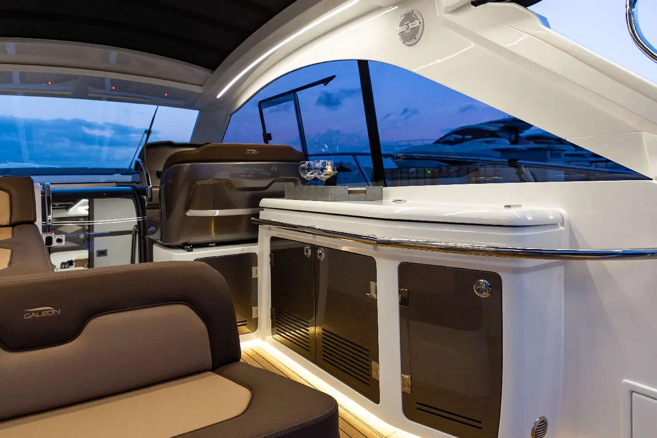 Interior of a yacht featuring modern seating, a sleek bar area, and large windows showcasing a twilight sky.
