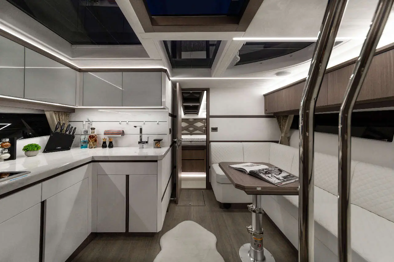 Modern boat interior featuring a sleek kitchen, dining area, white furnishings, and a large window with natural light.