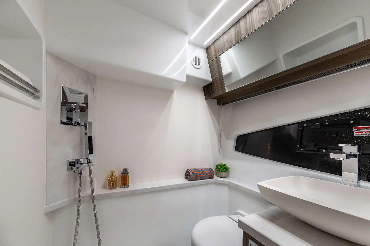 Modern boat bathroom with a sleek shower, sink, decorative plants, and stylish storage, featuring warm lighting and clean lines.
