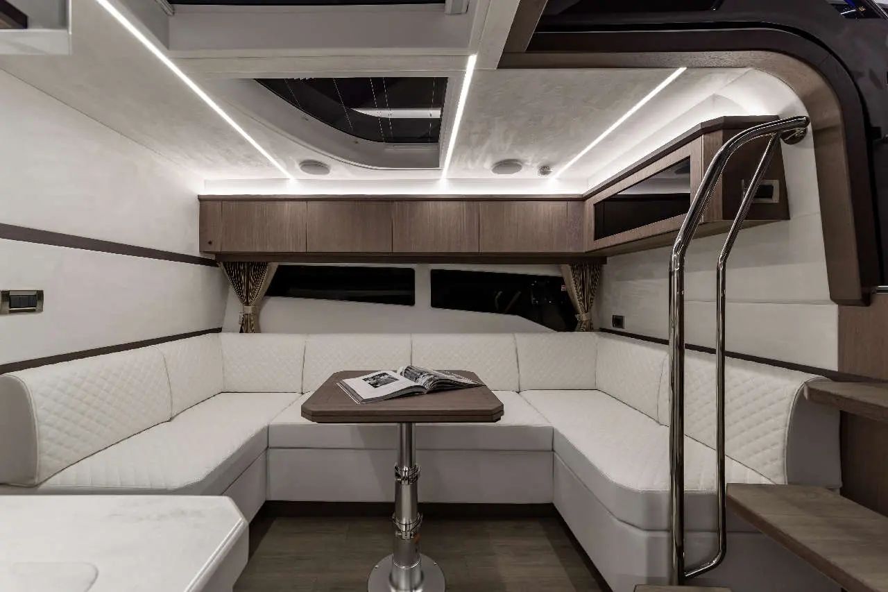 Modern boat interior featuring a white leather seating area, a wooden table, and ambient lighting, ideal for relaxation.