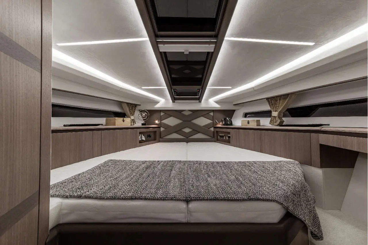 Modern boat interior featuring a double bed with a gray blanket and sleek wooden cabinetry, illuminated by ambient lighting.