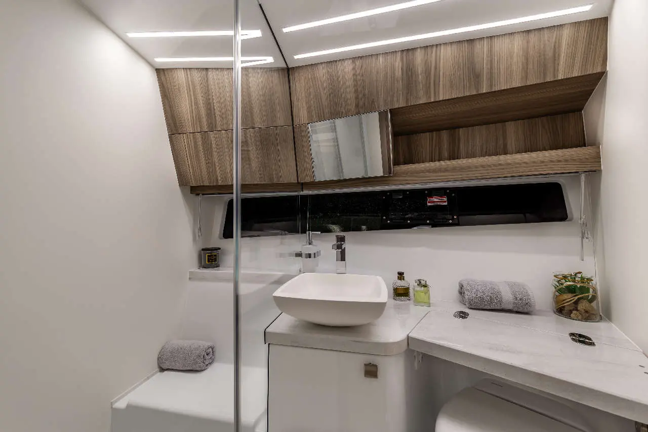Modern bathroom featuring a glass shower, wooden cabinets, a white sink, towels, and decorative toiletries on a marble counter.