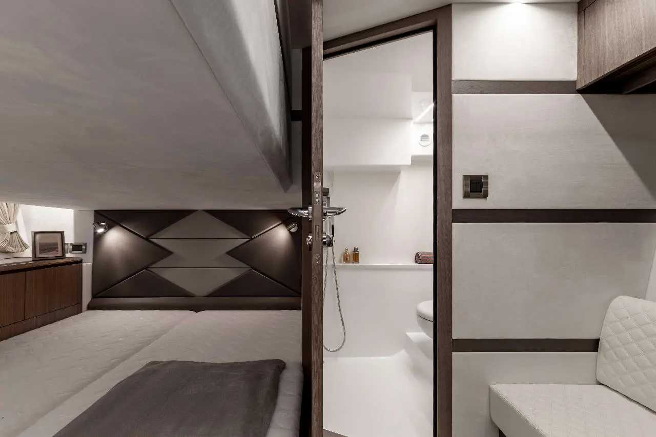 Modern yacht cabin interior with twin beds, a bathroom visible through a door, and sleek wood accents.