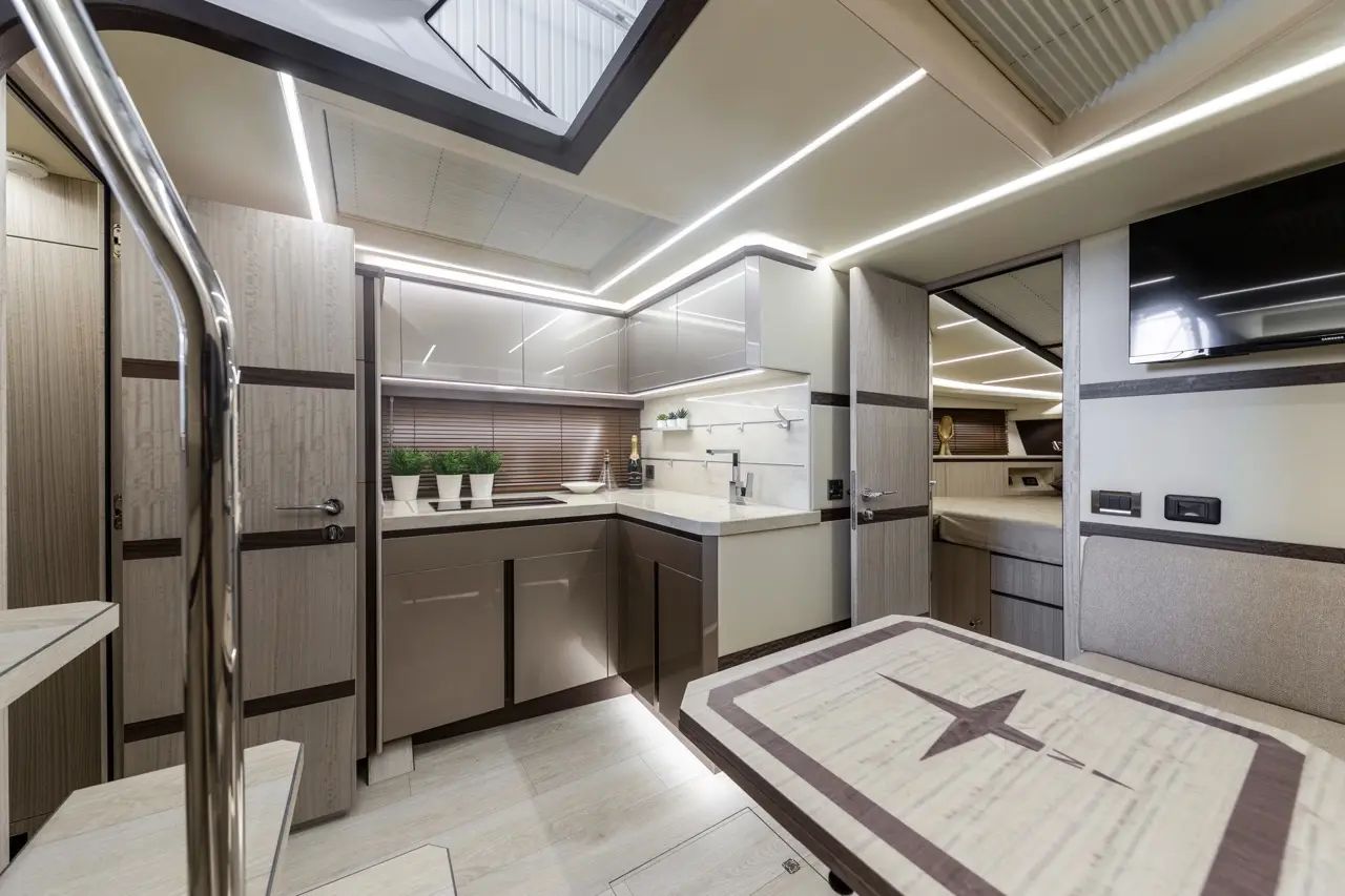 Modern yacht interior with a sleek kitchen, dining area, and light wood finishes; features cabinets, plants, and TV.