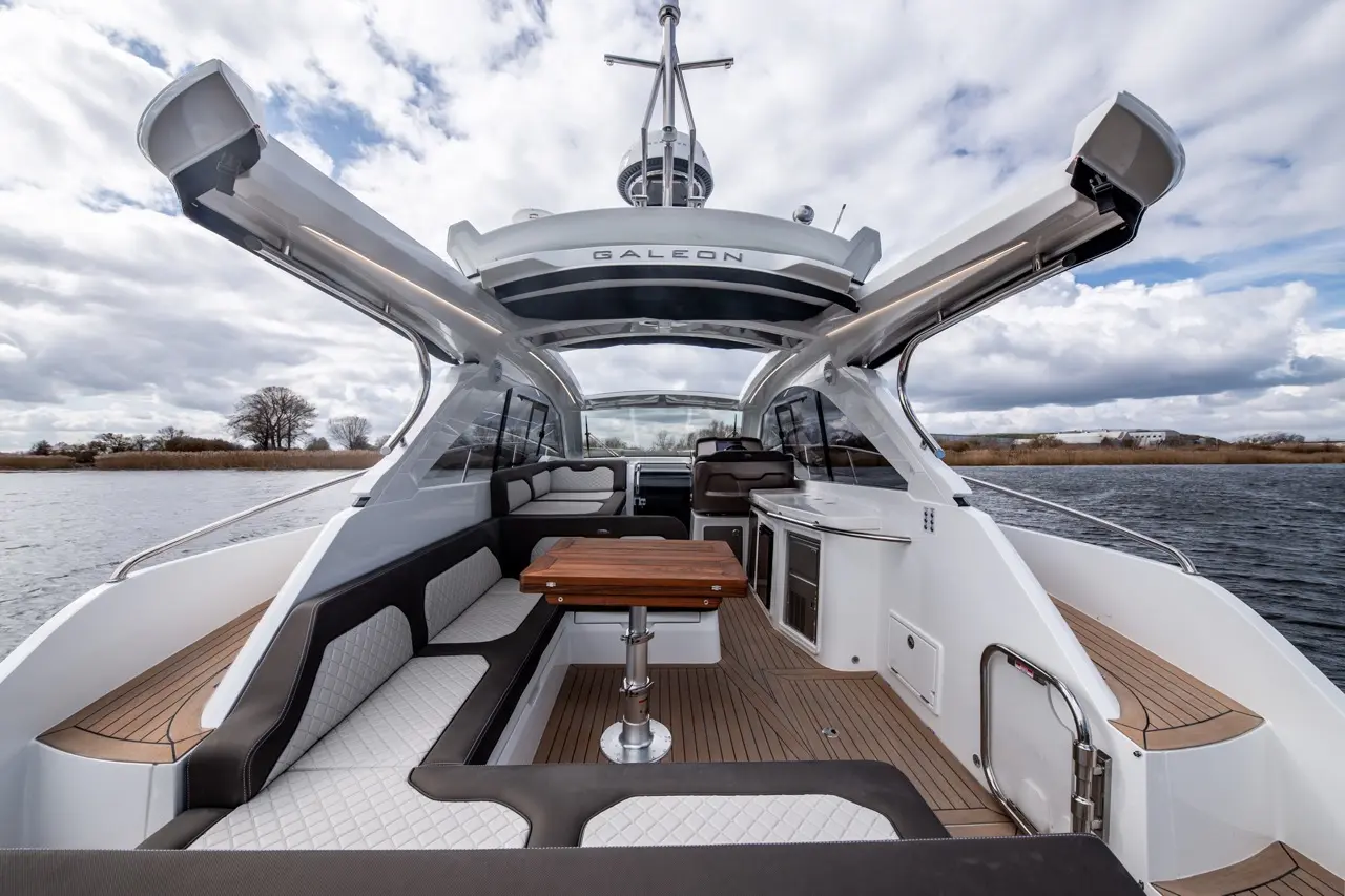 Interior of a Galeon yacht showcasing a stylish seating area, wooden table, panoramic windows, and a river view under cloudy skies.
