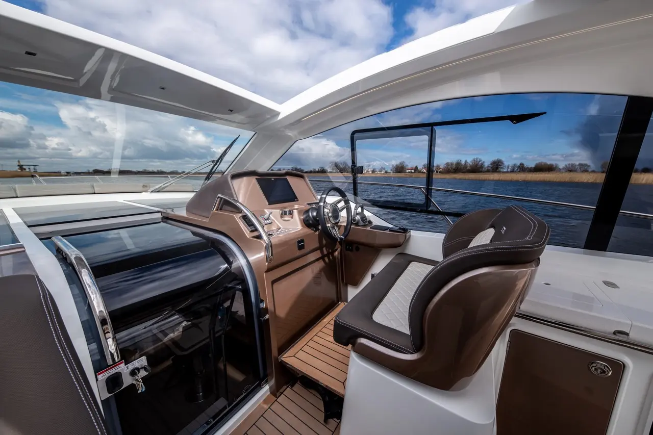 Sleek yacht interior featuring a modern helm, steering wheel, and view of water and sky through large windows.