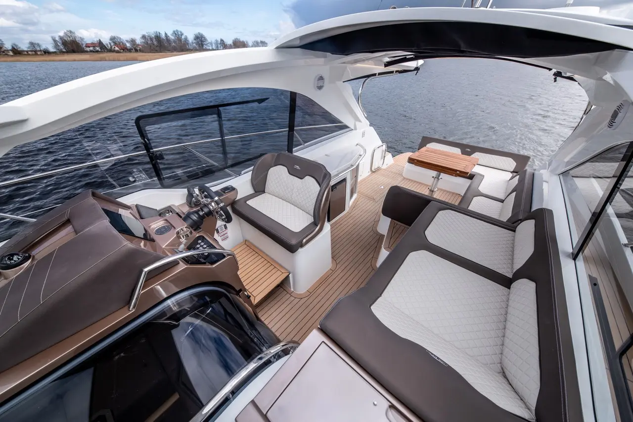 Luxury boat interior with a steering console, plush seating, and a scenic water view, featuring wood detailing on the floor.
