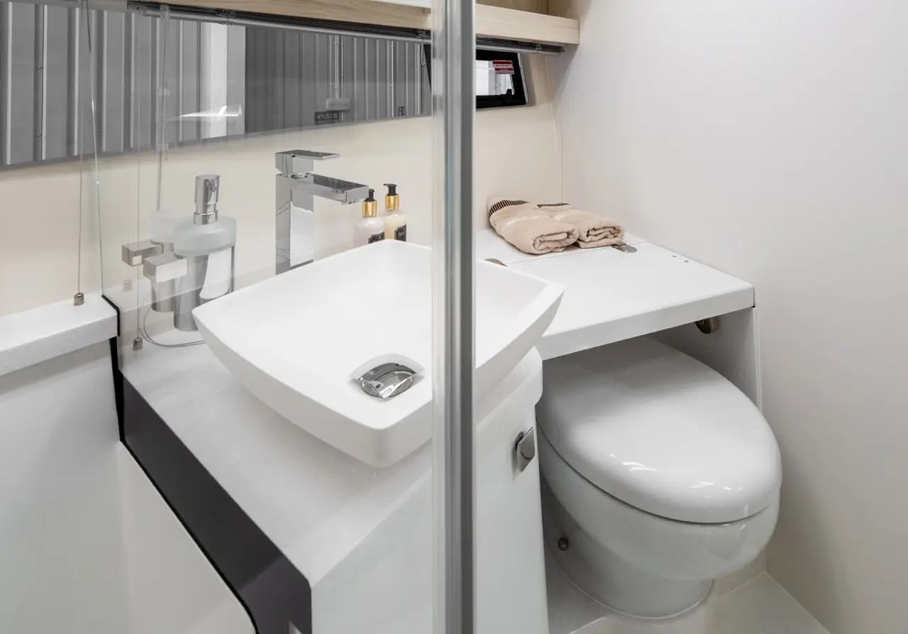 Modern bathroom featuring a white sink, chrome tap, toiletries, towels, and a sleek toilet, designed for efficiency and style.