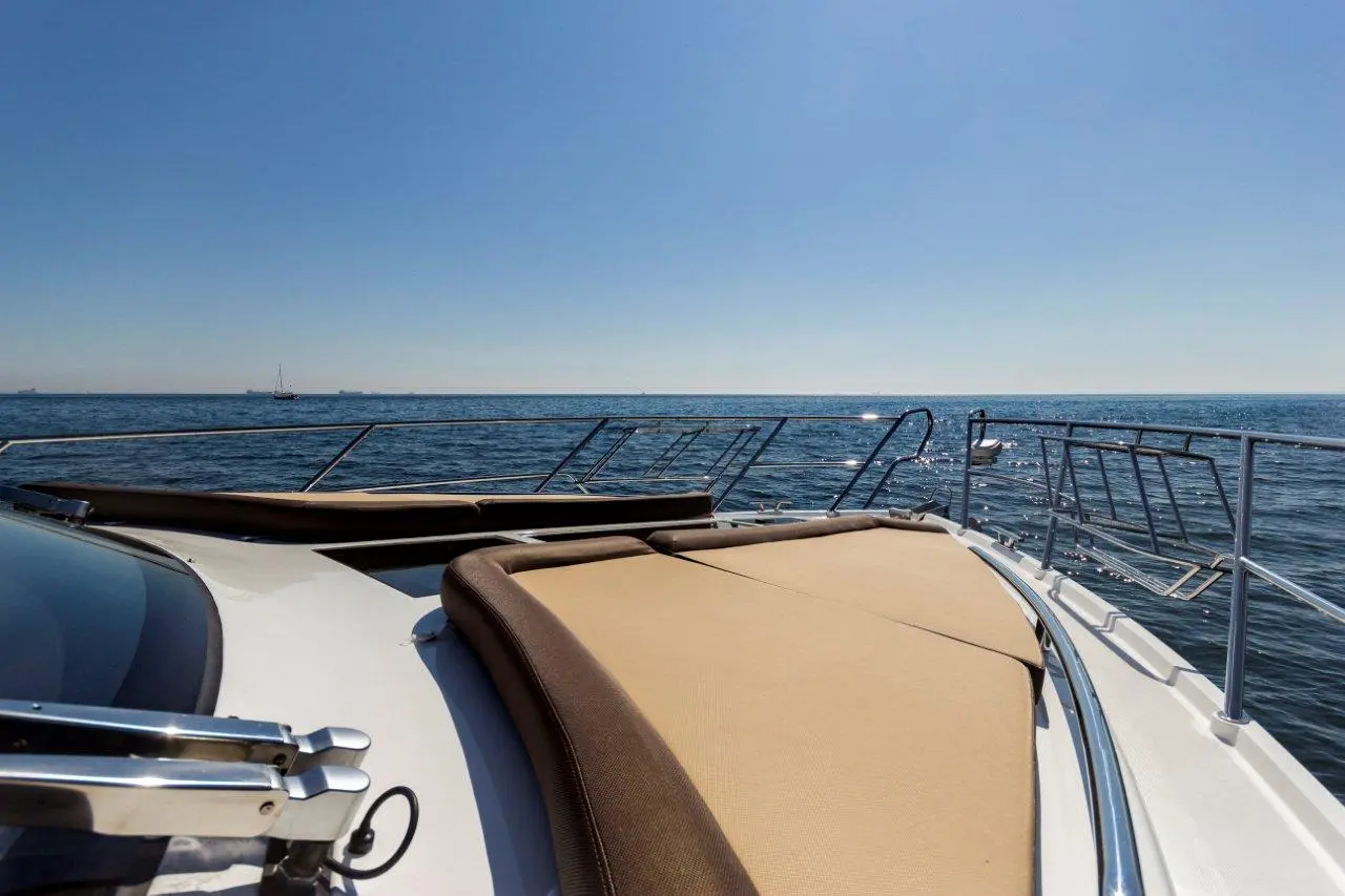 View from a yacht’s deck, featuring a sunbathing area and a clear blue sea, with distant boats and a bright sky.