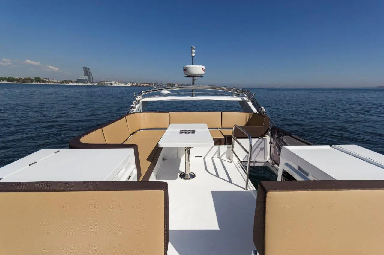A spacious yacht deck featuring beige seating, a table, and views of water and city skyline under a clear blue sky.
