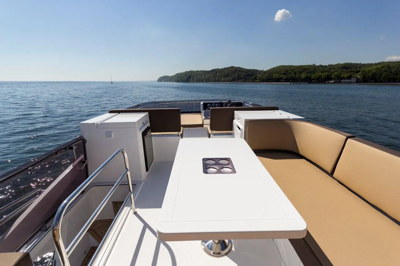 Luxury boat deck with beige seating, a white table, and a view of calm water and green hills under a clear blue sky.