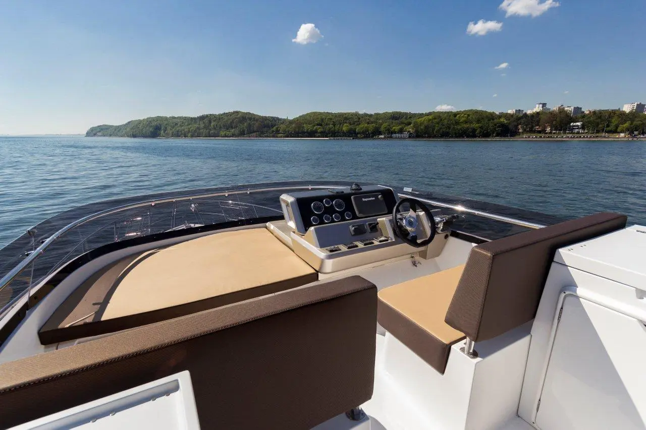 View from the helm of a luxury boat, showcasing the dashboard and comfortable seating with water and lush hills in the background.