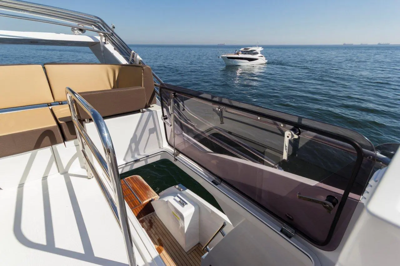 View from a boat showing cushioned seating, a wooden deck, and another yacht in the calm water on a clear day.