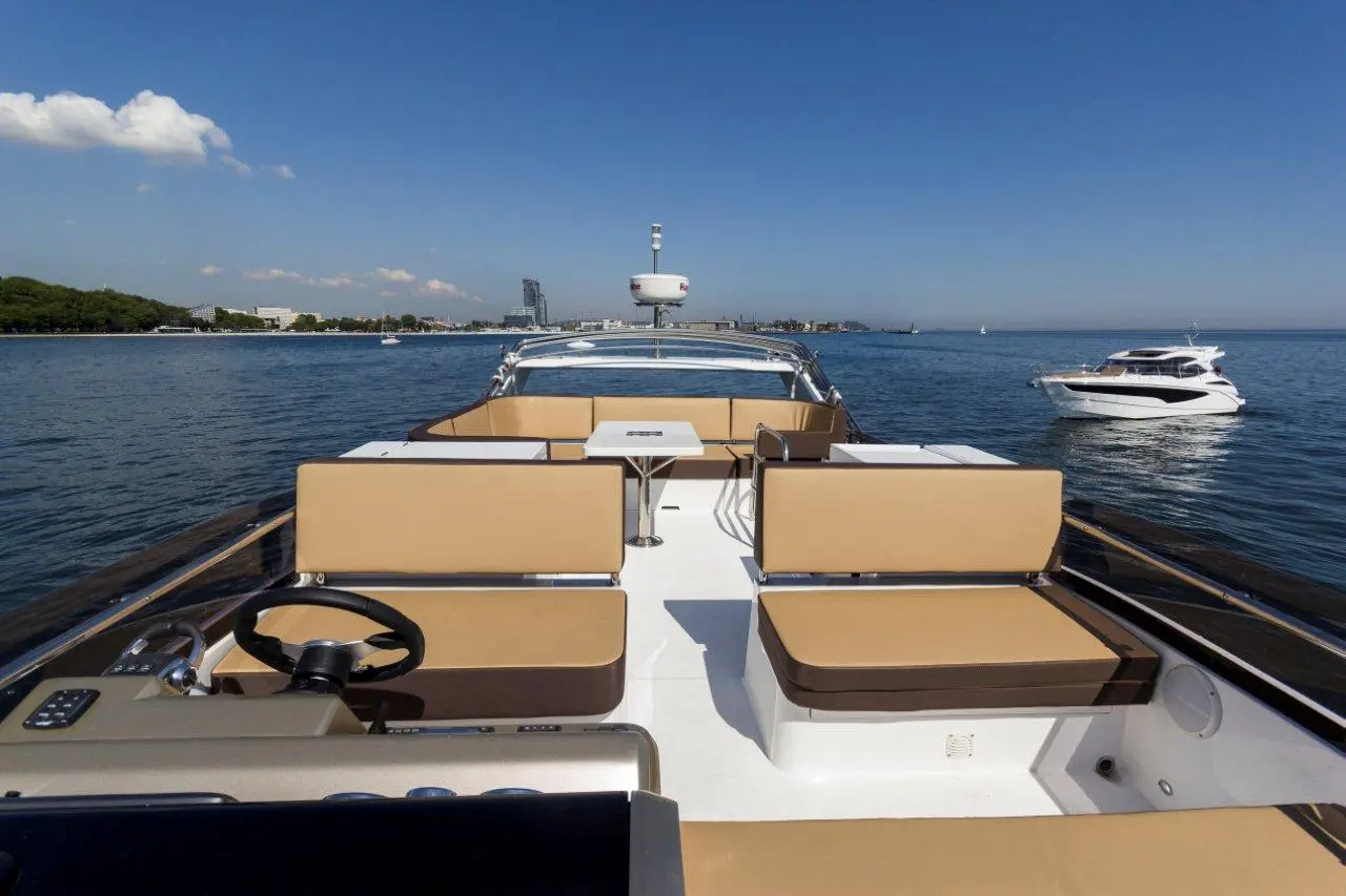 View from the deck of a luxury yacht, featuring tan seating, a steering wheel, and another boat in calm waters.