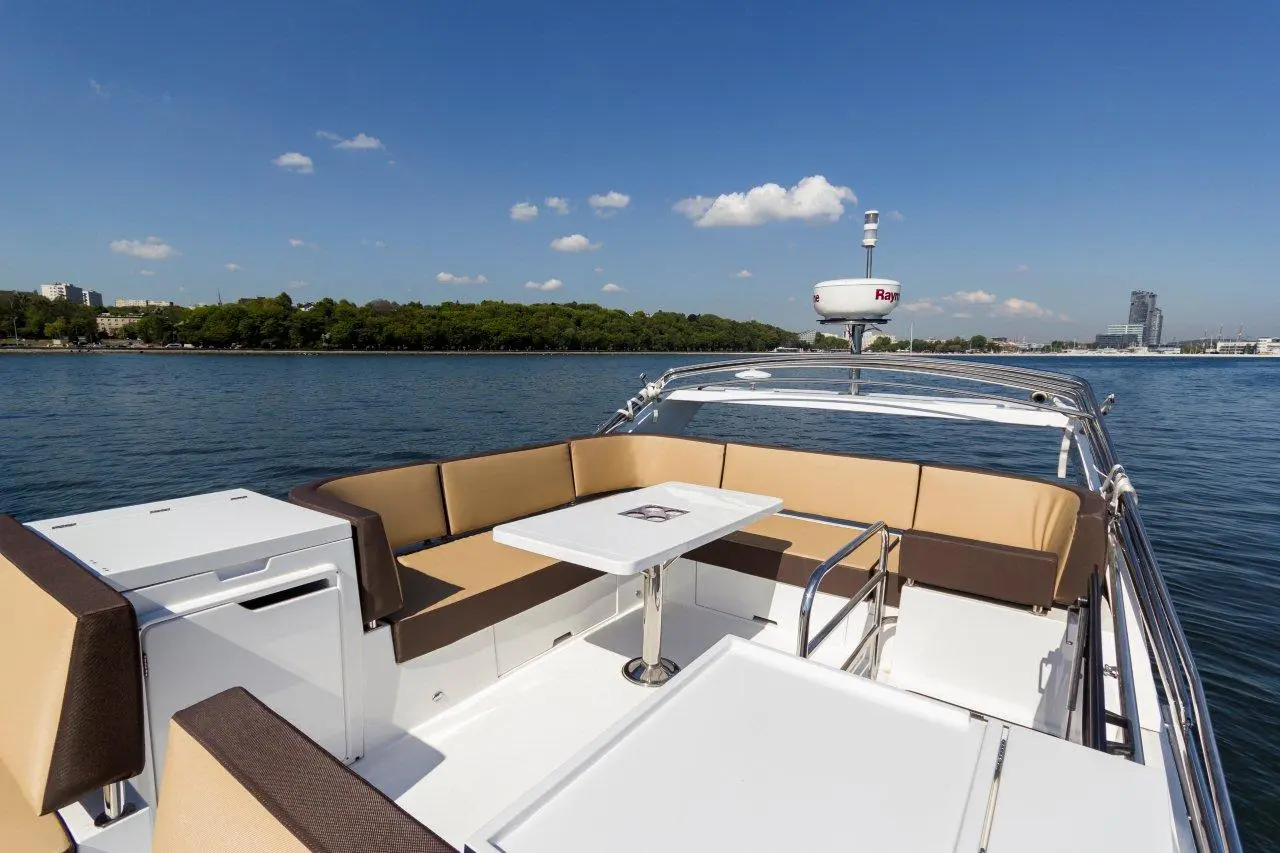 A luxury boat deck with cushioned seating, a table, and lake view under a clear blue sky with a few clouds.