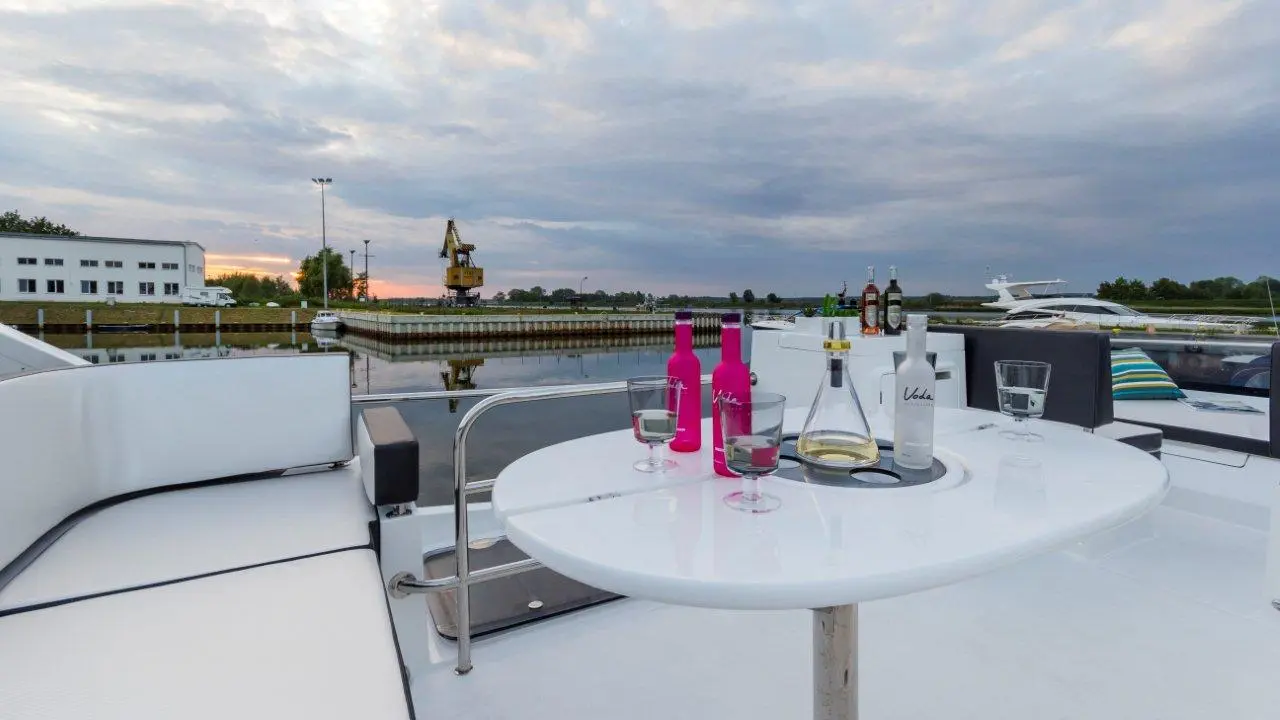 Outdoor yacht bar scene featuring colorful beverage bottles, glasses, and a scenic waterfront view at sunset.