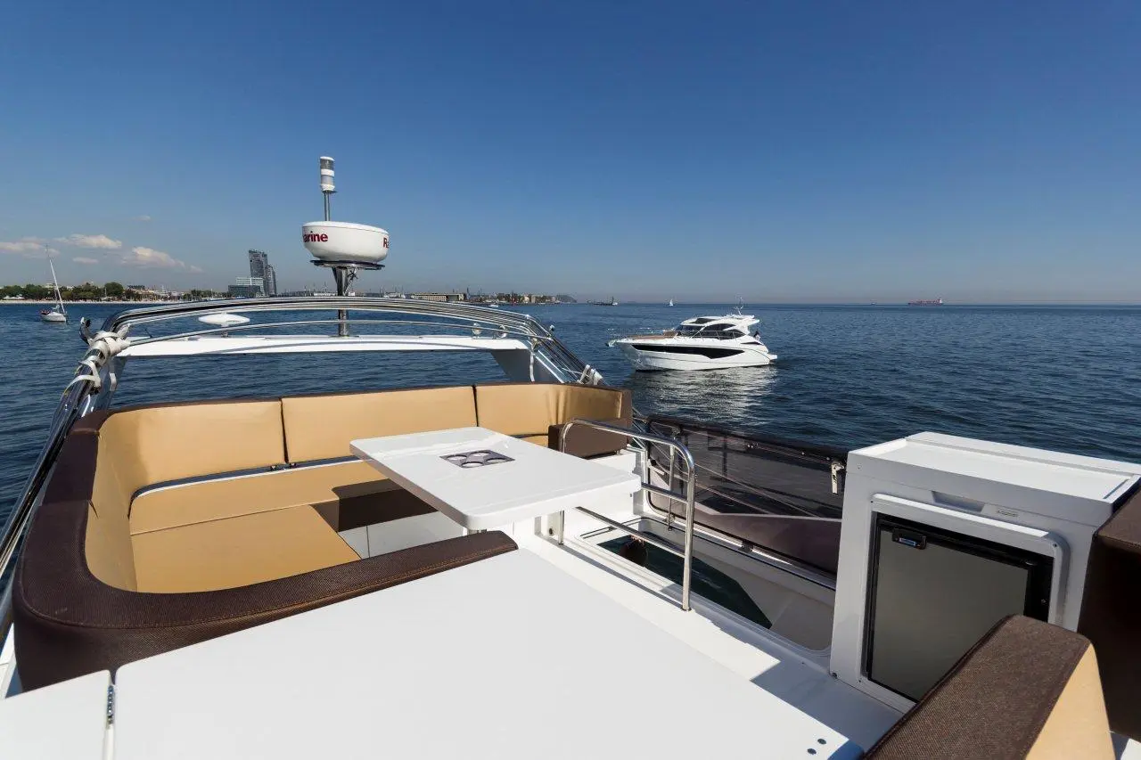 Luxury yacht deck with seating and table, overlooking calm waters and another boat, under a clear blue sky.