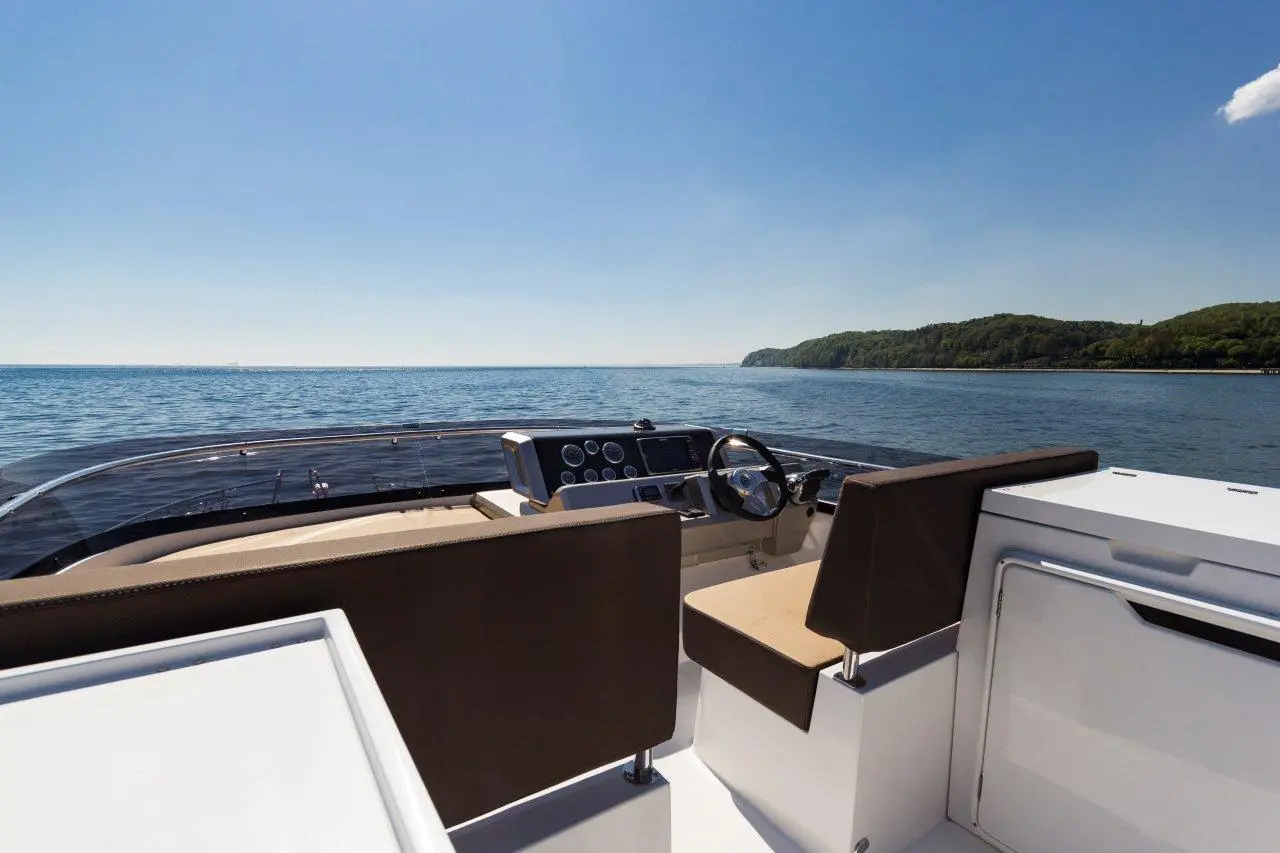 Stylish yacht interior with a clear view of calm water and a lush green coastline under a sunny blue sky.