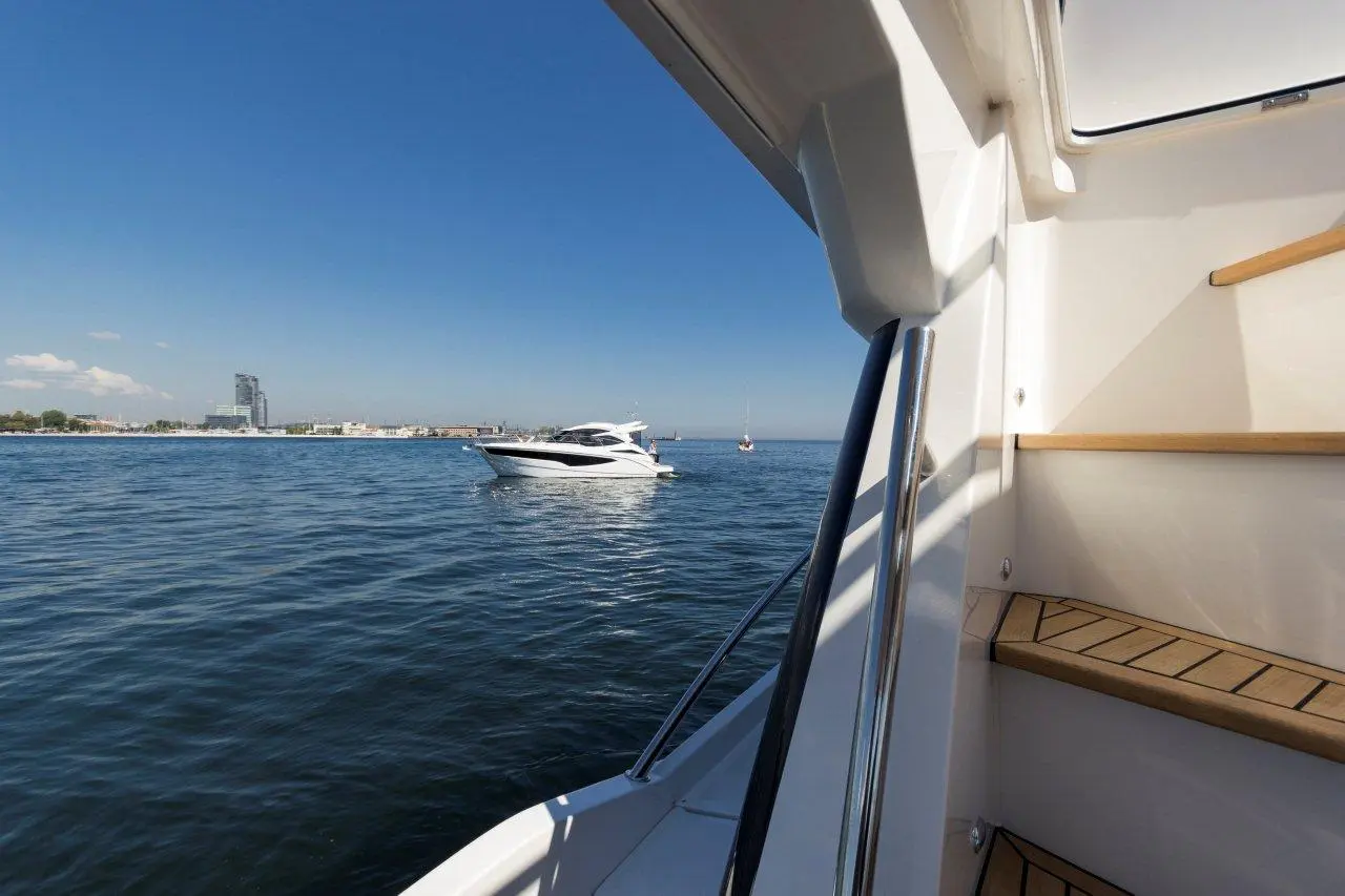View from a boat showing calm waters, a nearby yacht, and a city skyline under a clear blue sky.