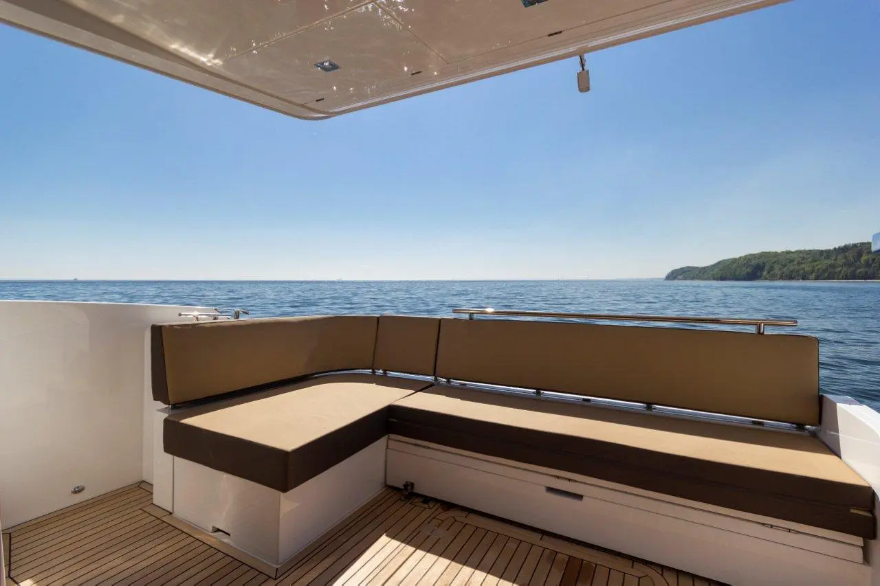 A comfortable seating area on a boat overlooks calm waters and greenery under a clear blue sky.