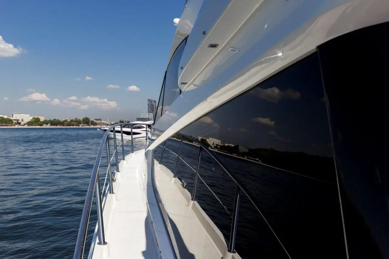 Luxury yacht profile sailing on calm waters with a skyline in the background under a clear blue sky.