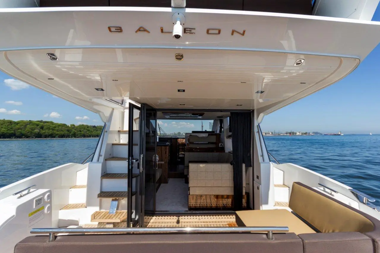 Interior view of a Galleon yacht showing a spacious lounge, stairs, and scenic water backdrop under a clear sky.