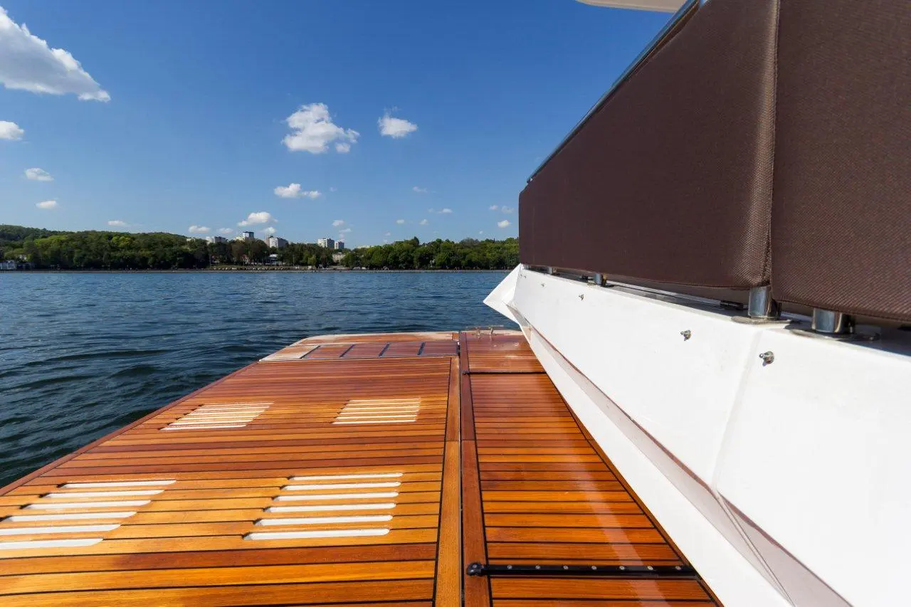 View from a boat deck overlooking calm water, green landscape, and a distant city skyline under a blue sky with clouds.