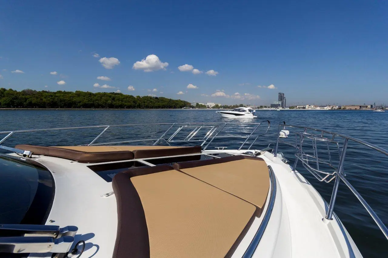 View from a luxury boat's deck showcasing a calm waterway with green shoreline and a distant yacht under a blue sky.