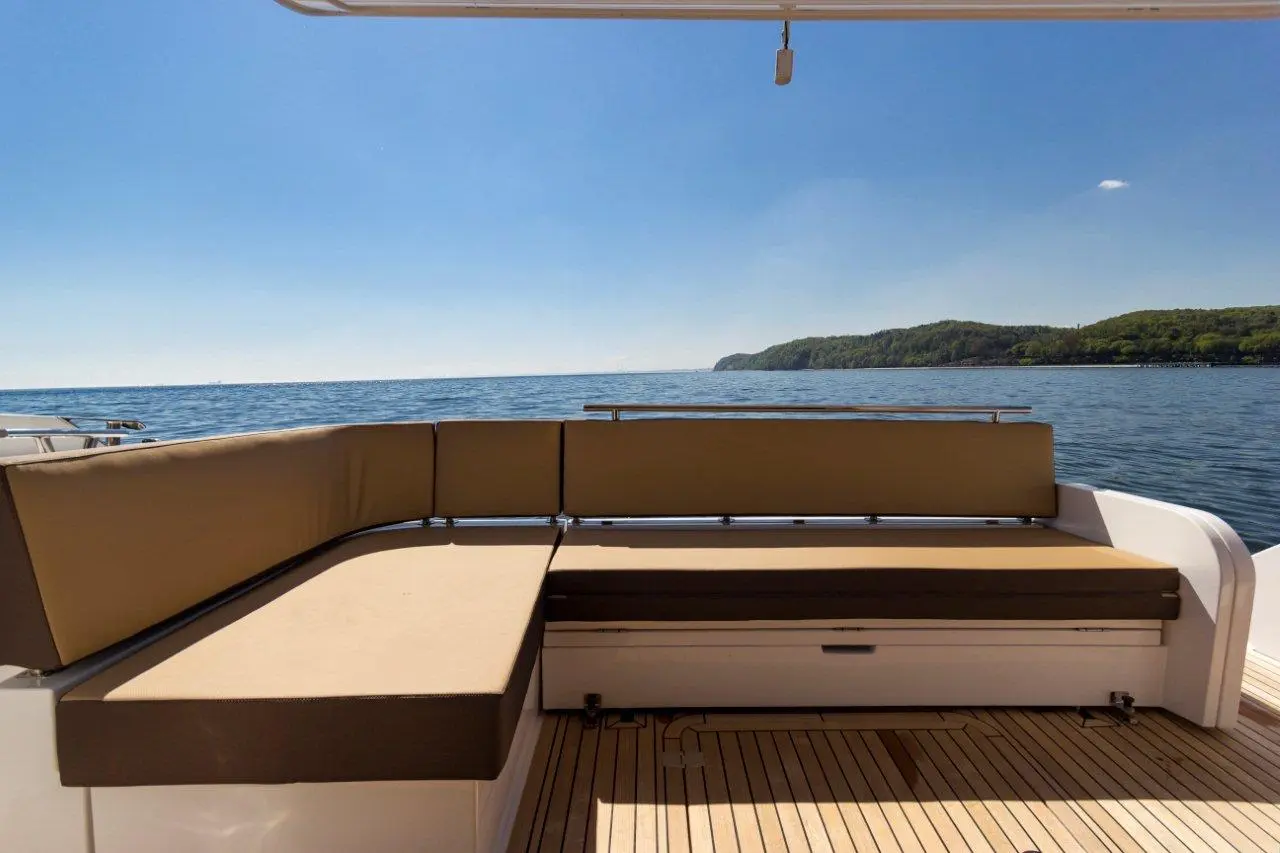 Spacious boat deck with cushioned seating, overlooking calm waters and a green hillside under a clear blue sky.