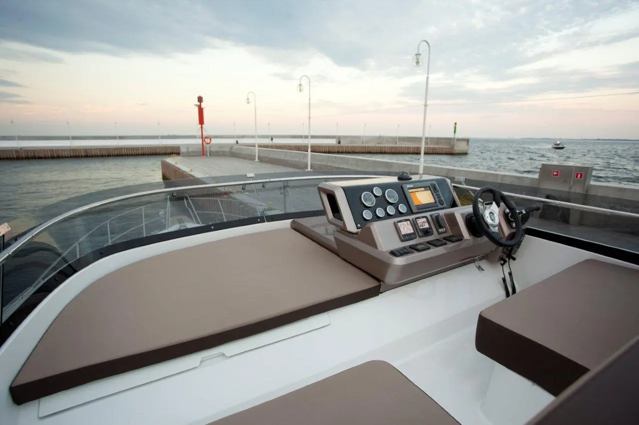 View from a boat's helm showcasing the dashboard, controls, and the sea with a dock in the background.